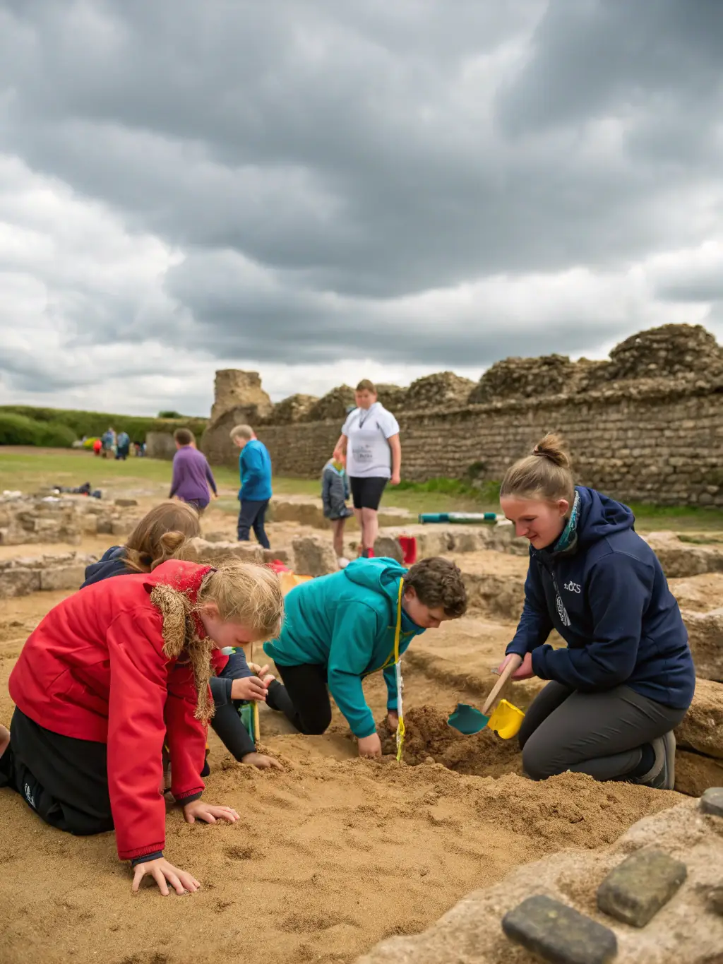 A group of children participating in an archeological dig activity at the Château de la Hunaudaye, supervised by association members, showcasing the educational aspect of the program.